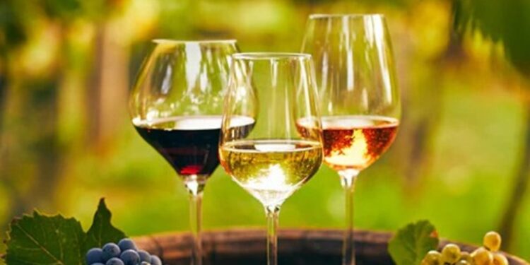 Tre calici di vino con sullo sfondo un vigneto