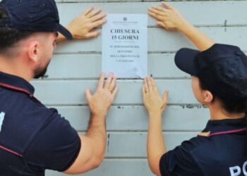 Due poliziotti affiggono i sigilli con il provvedimento di chiusura per 15 giorni