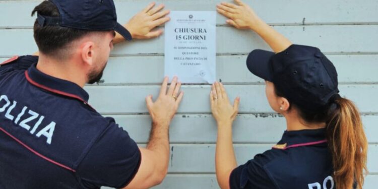 Due poliziotti affiggono i sigilli con il provvedimento di chiusura per 15 giorni