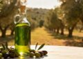 Una bottiglia di olio extravergine d'oliva con sullo sfondo degli ulivi e sul tavolo delle olive