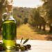 Una bottiglia di olio extravergine d'oliva con sullo sfondo degli ulivi e sul tavolo delle olive