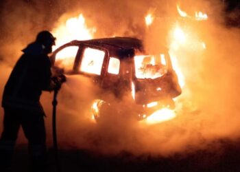 I vigili del fuoco cercano di spegnere un'auto data alle fiamme
