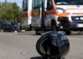 Un casco sull'asfalto e una ambulanza sul luogo di un incidente