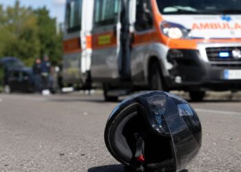 Un casco sull'asfalto e una ambulanza sul luogo di un incidente