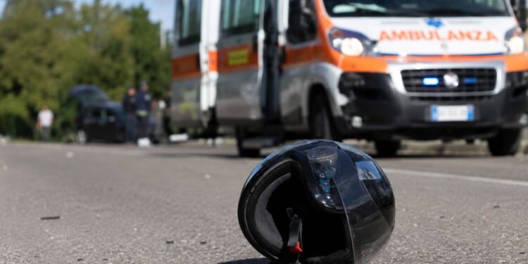 Un casco sull'asfalto e una ambulanza sul luogo di un incidente